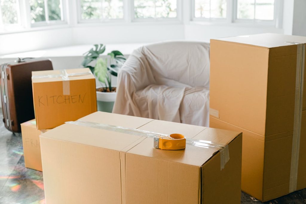 Cardboard boxes labeled Kitchen in sunlit living room, ready for relocation.